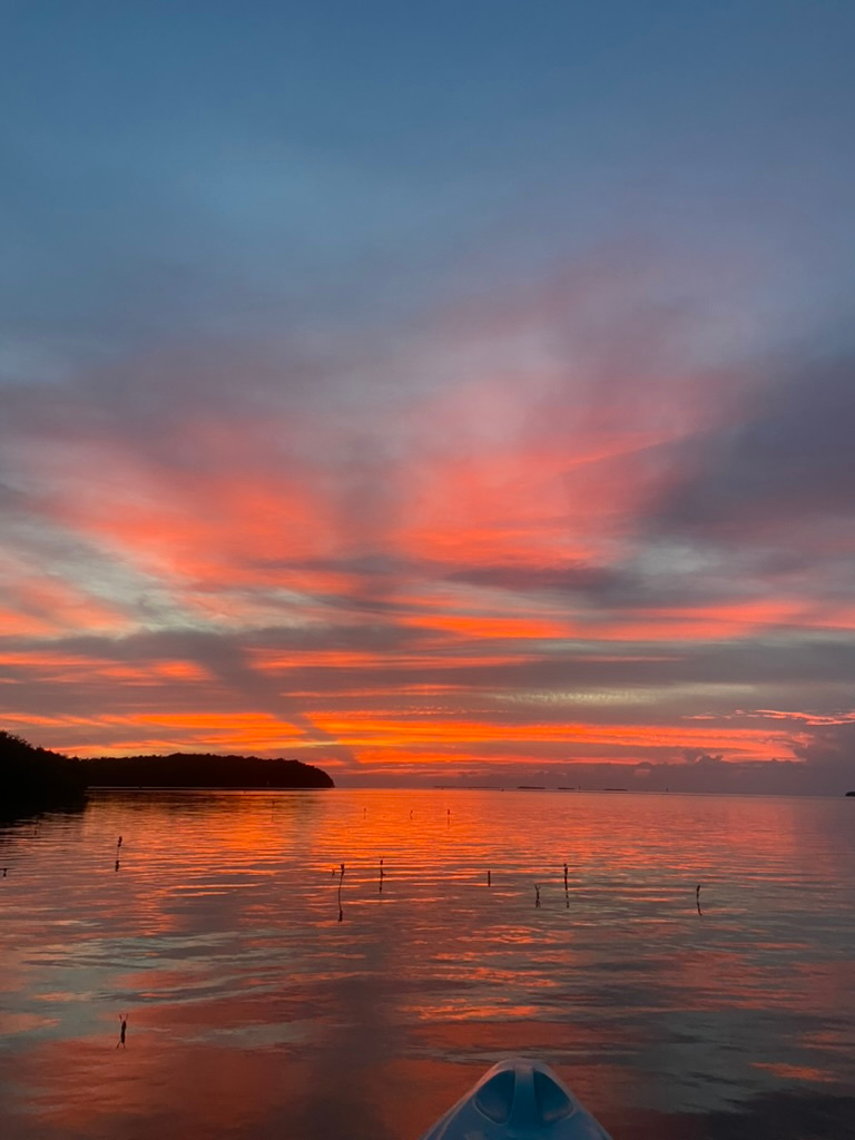 Vibrant sunset over calm water, orange and pink sky reflecting on the surface.