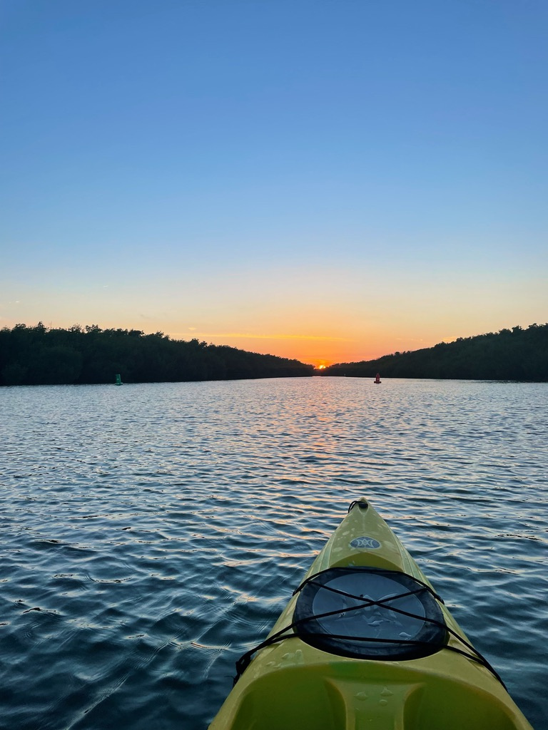 Kayak on a calm river at sunset with trees on both sides.