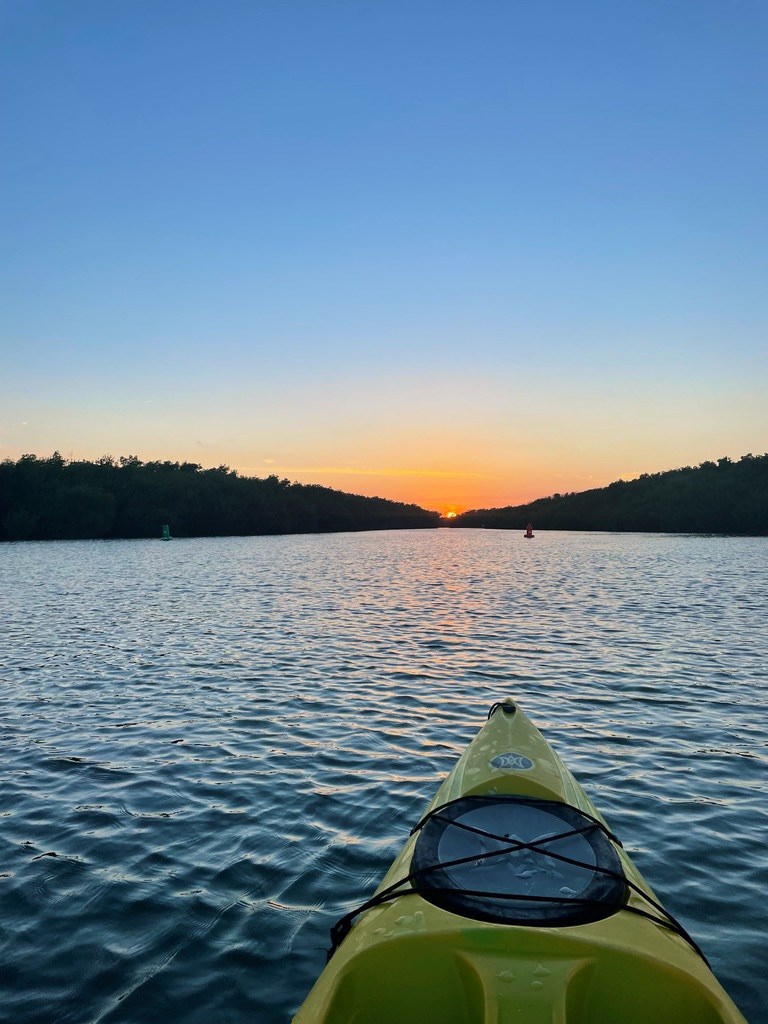 Kayak on a calm river at sunset with trees on both sides.