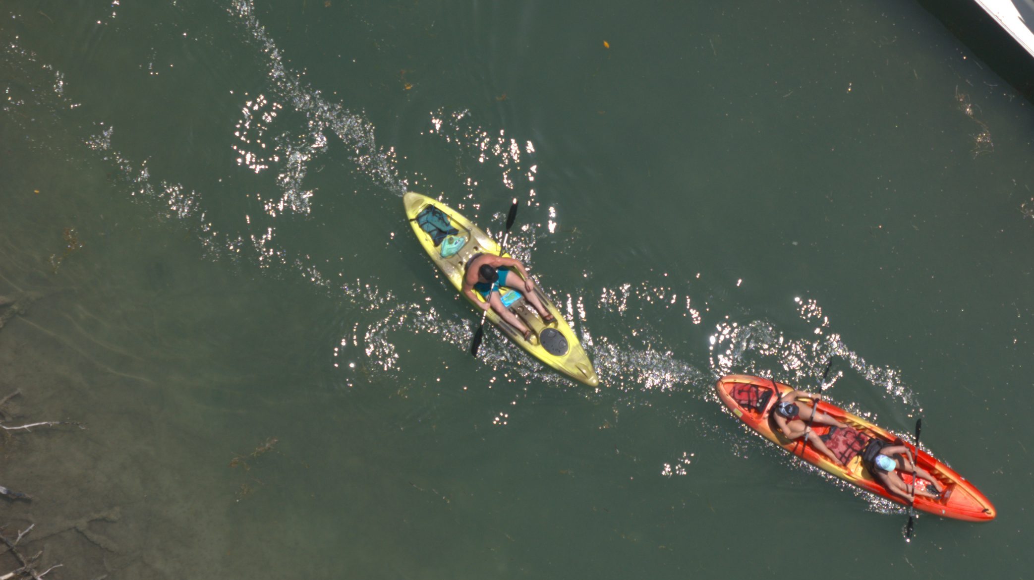Two kayaks on a river with paddlers, viewed from above.