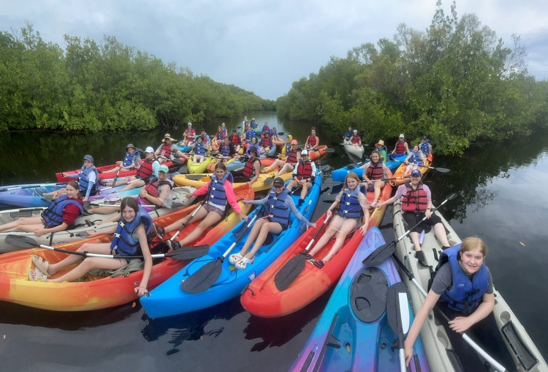 Group of people in colorful kayaks on a narrow waterway with surrounding greenery.