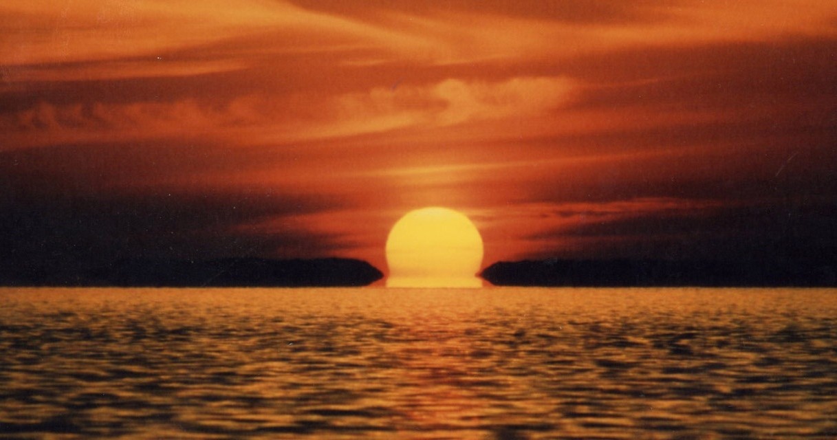 Sunset over the ocean with vibrant orange sky and reflection on water.