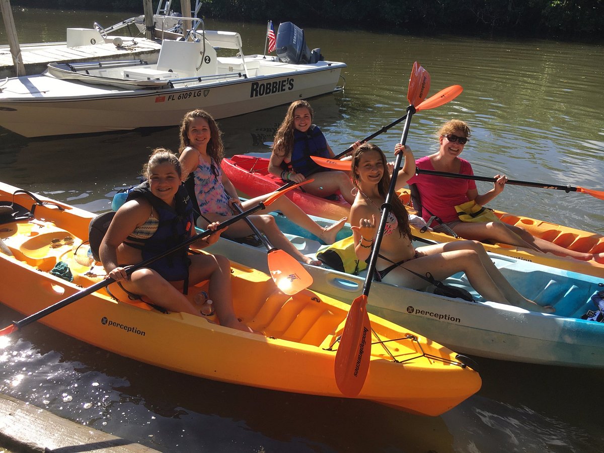 Group of smiling people in kayaks on a sunny day near a docked boat.